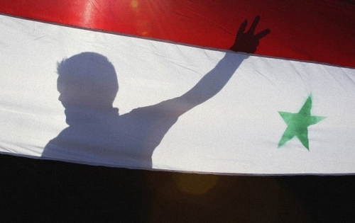 A_Syrian_protester_is_silhouetted_behind_a_Syrian_flag
